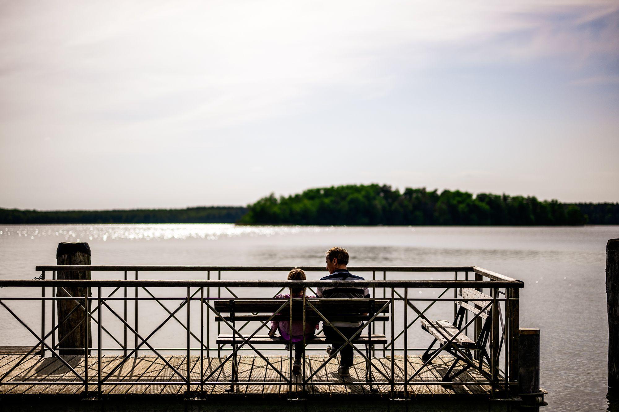 Zwei Personen sitzen auf einer Bank auf einem Steg und schauen auf das Wasser