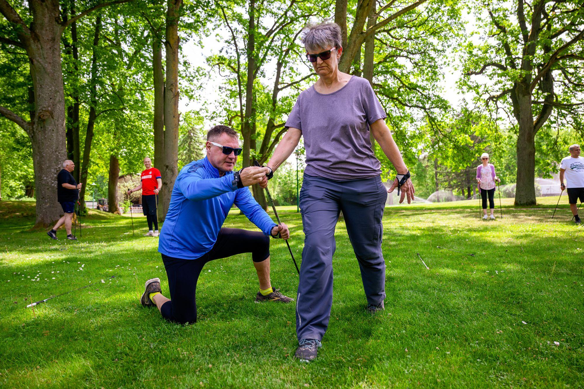 Ein Therapeut zeigt einer Frau die richtige Nutzung von Nordic Walking Stöcken