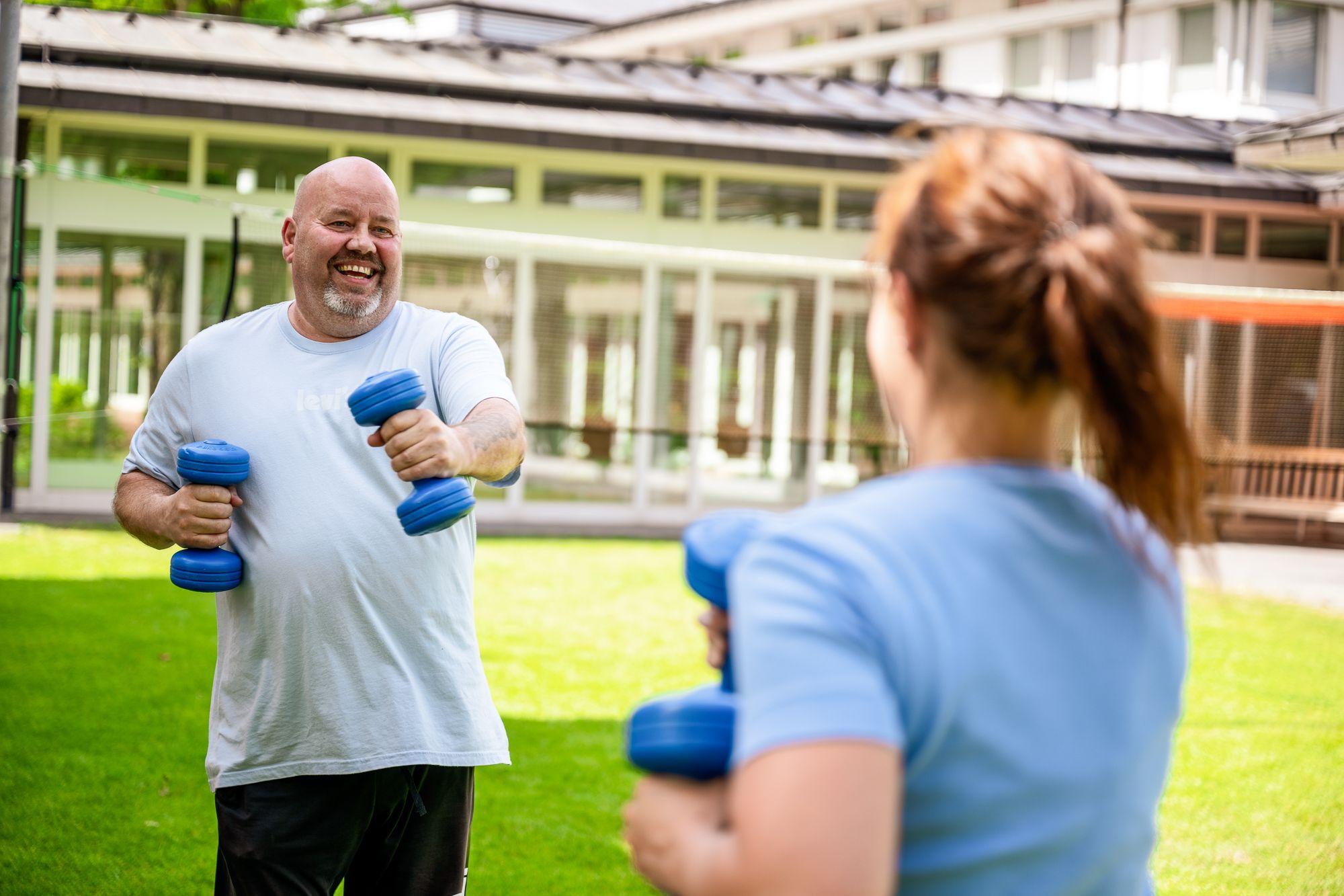 Ein Patient trainiert mit einer Therapeutin mit Kurzhanteln