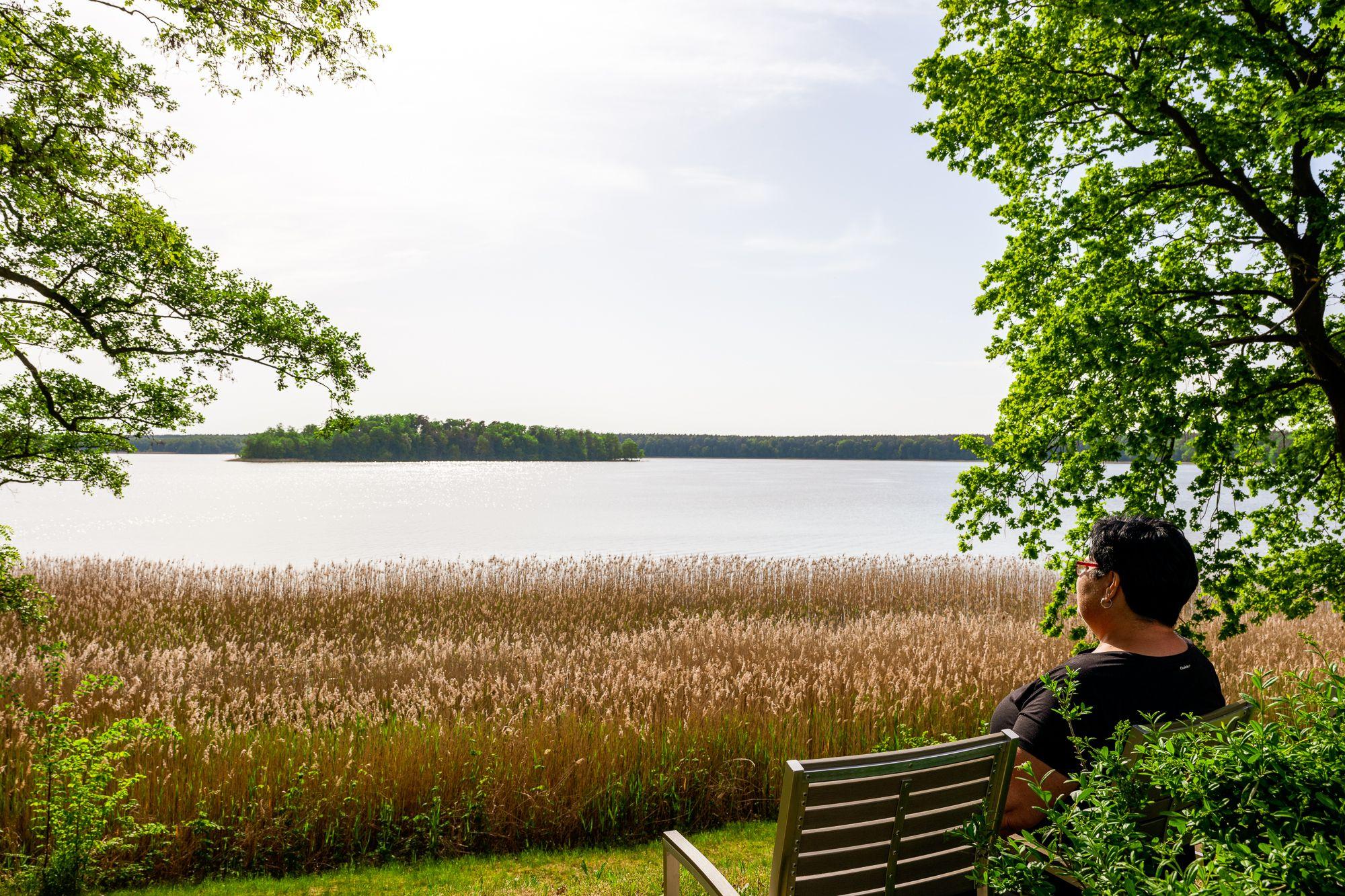 Ein Mann sitzt auf einer Bank und blickt auf den See vor ihm
