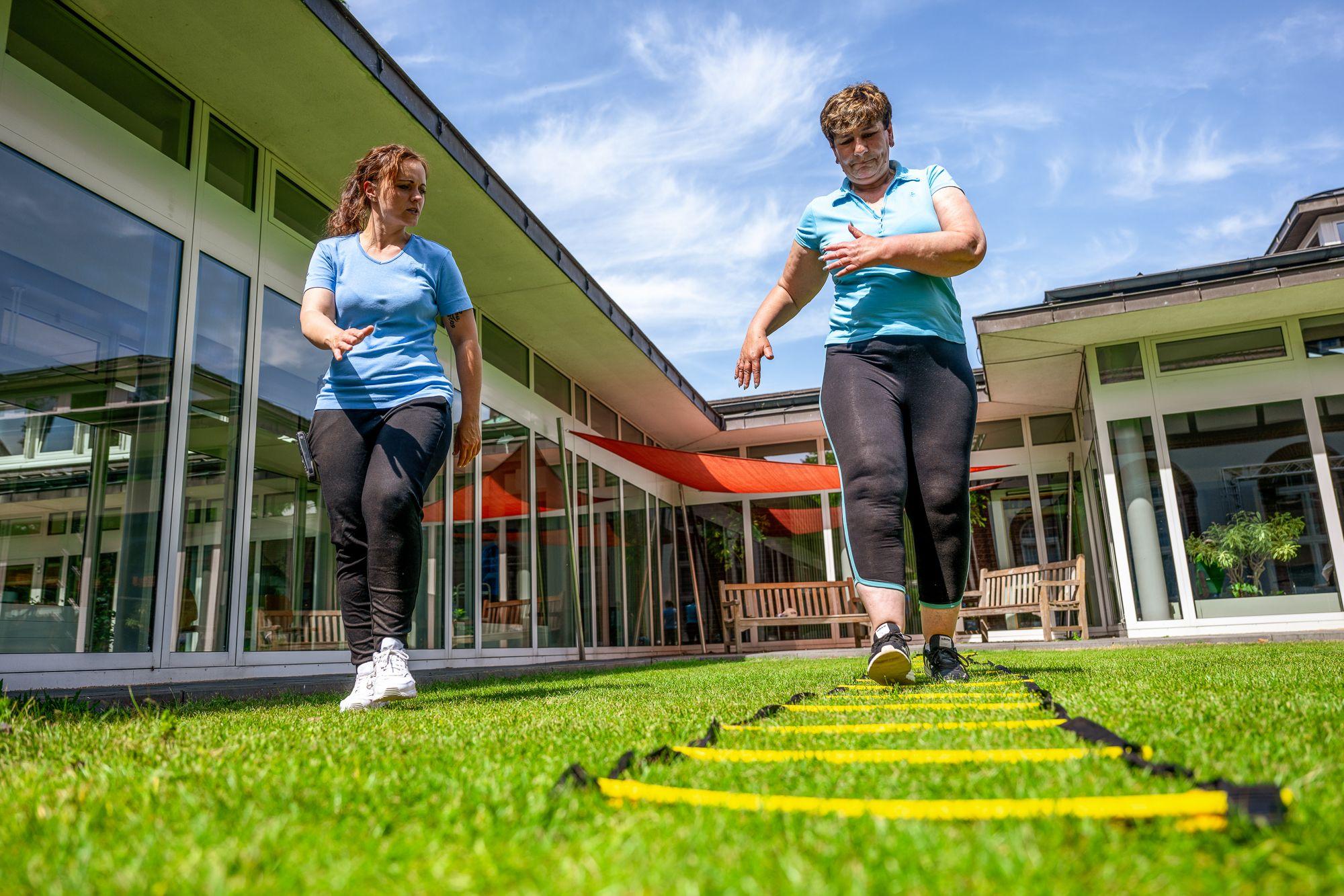 Trainerin übt mit einer Patientin an einer Koordinationsleiter